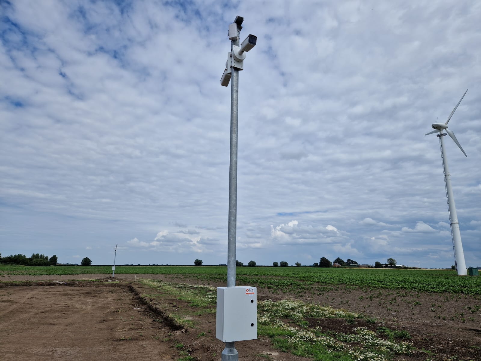 Image of a CCTV camera system in a field, next to a wind turbine
