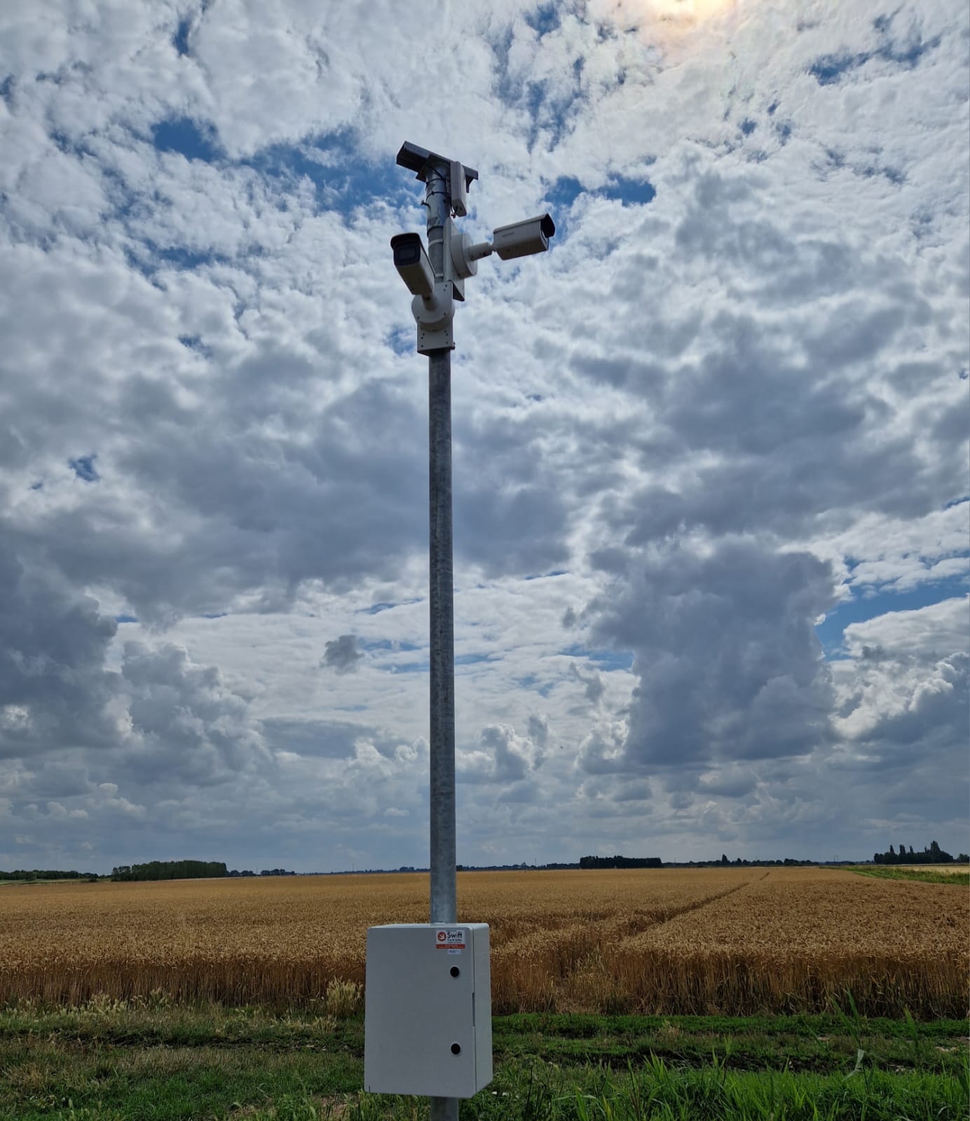 A pole with three CCTV cameras surveying nearby land, just outside a corn field